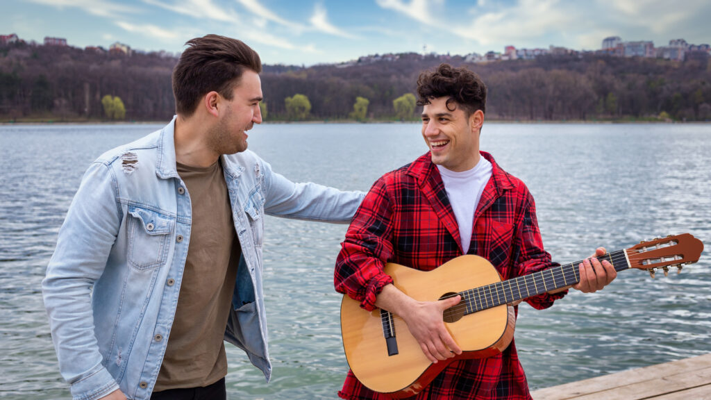 two young friends singing playing guitar near lake park